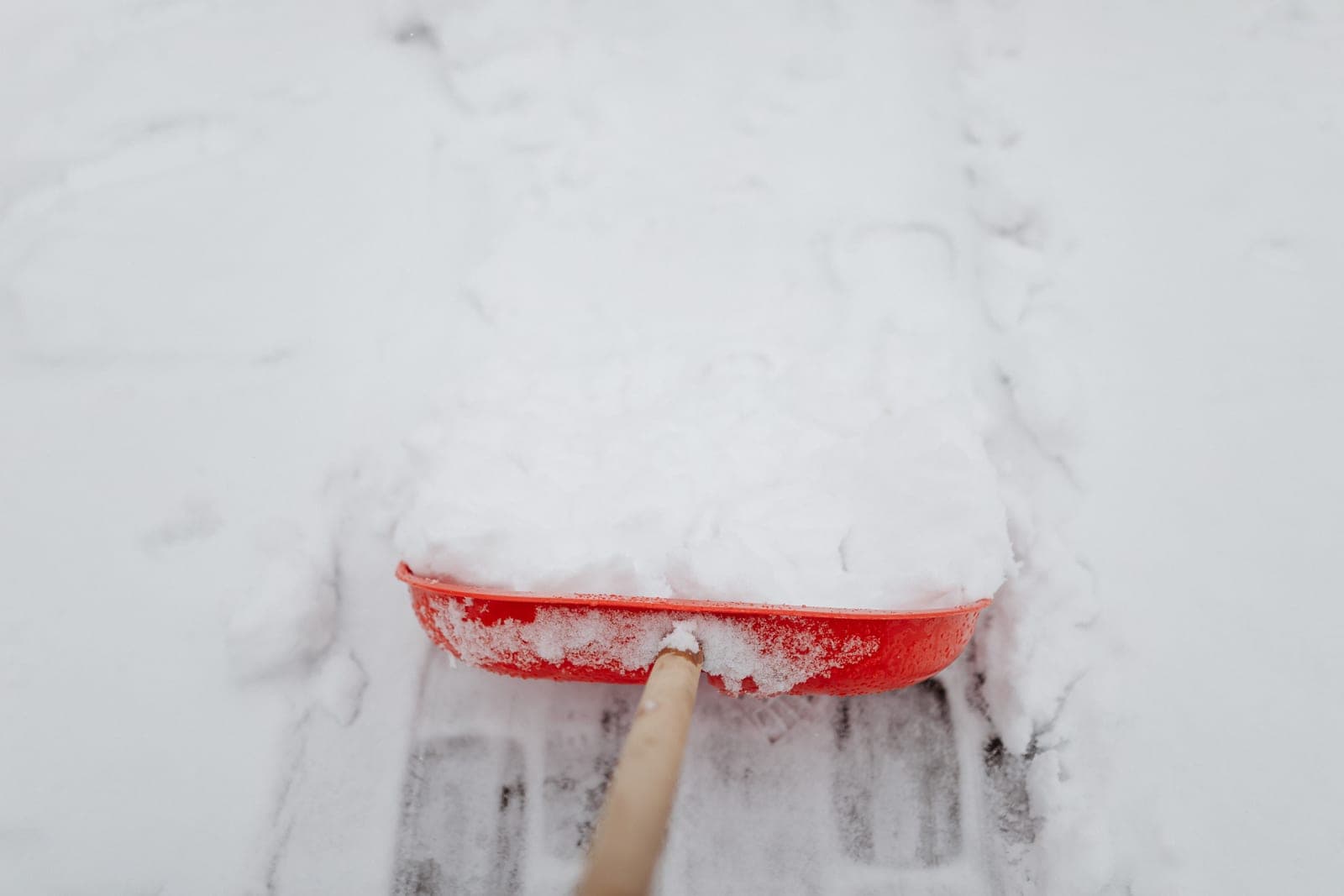 A snow shovel resting against a snowbank beside a partly cleared driveway