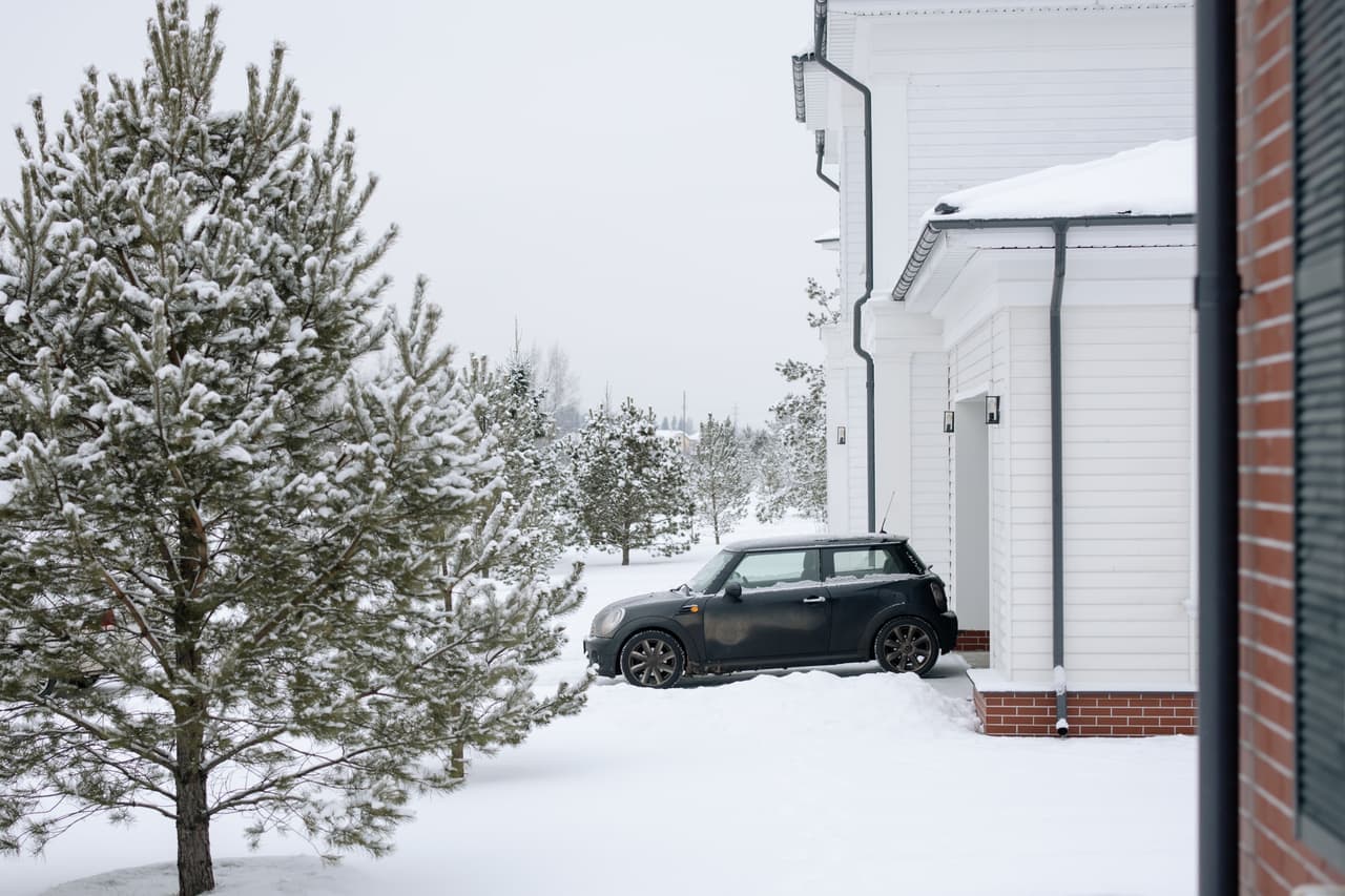 A long snow-covered driveway curving between snow-laden trees toward a house