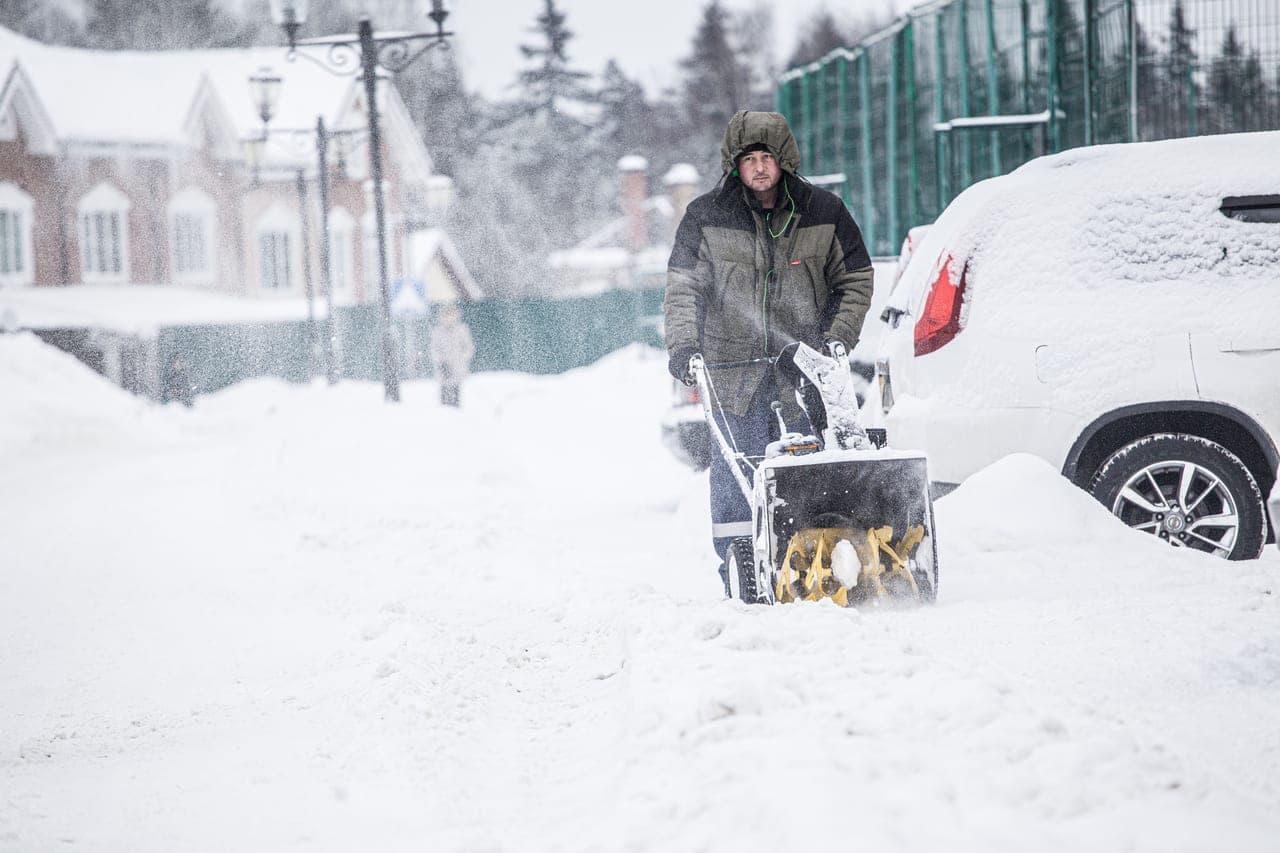 A snow blower throwing an arc of snow across a cleared driveway in winter light